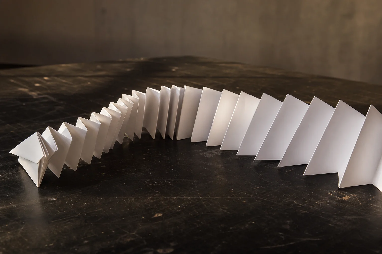 White folded paper panels form a curved line on a dark tabletop under warm light.